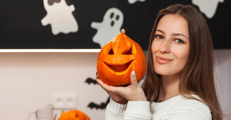 A young woman holding a pumpkin with eyes and mouth carved into it, showcasing her handiwork.