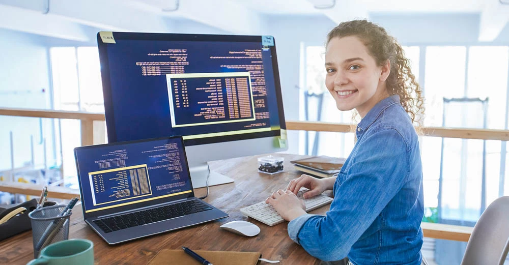 woman coding on two computer's