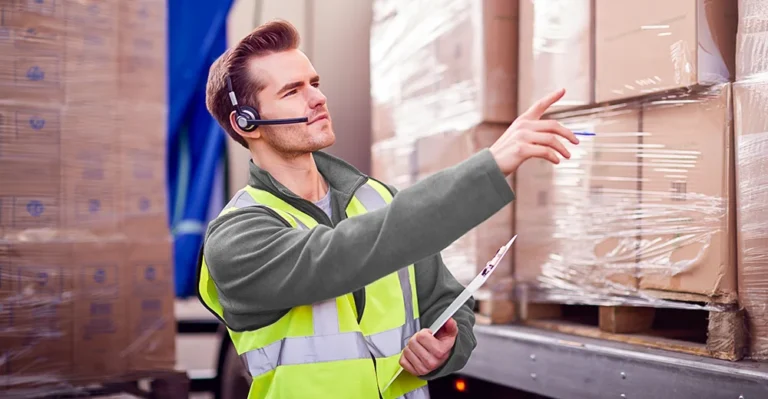 A logistics coordinator holding a clipboard, standing in front of a freight truck loaded with stacked shipping boxes