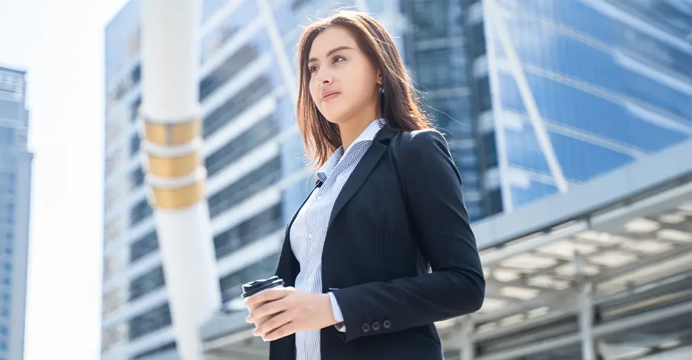 A smiling female newcomer to Canada walking through a downtown area surrounded by office buildings.