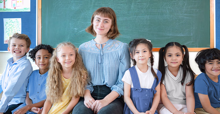 A woman sits next to a group of young students after becoming an education assistant.