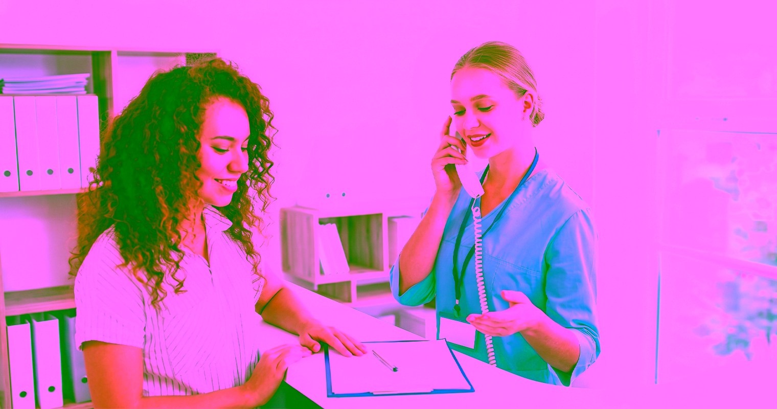 Medical office assistant helping a patient with check-in at the clinic reception desk.